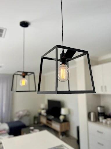 Black cage pendant lights with filament globes hanging over a kitchen bench