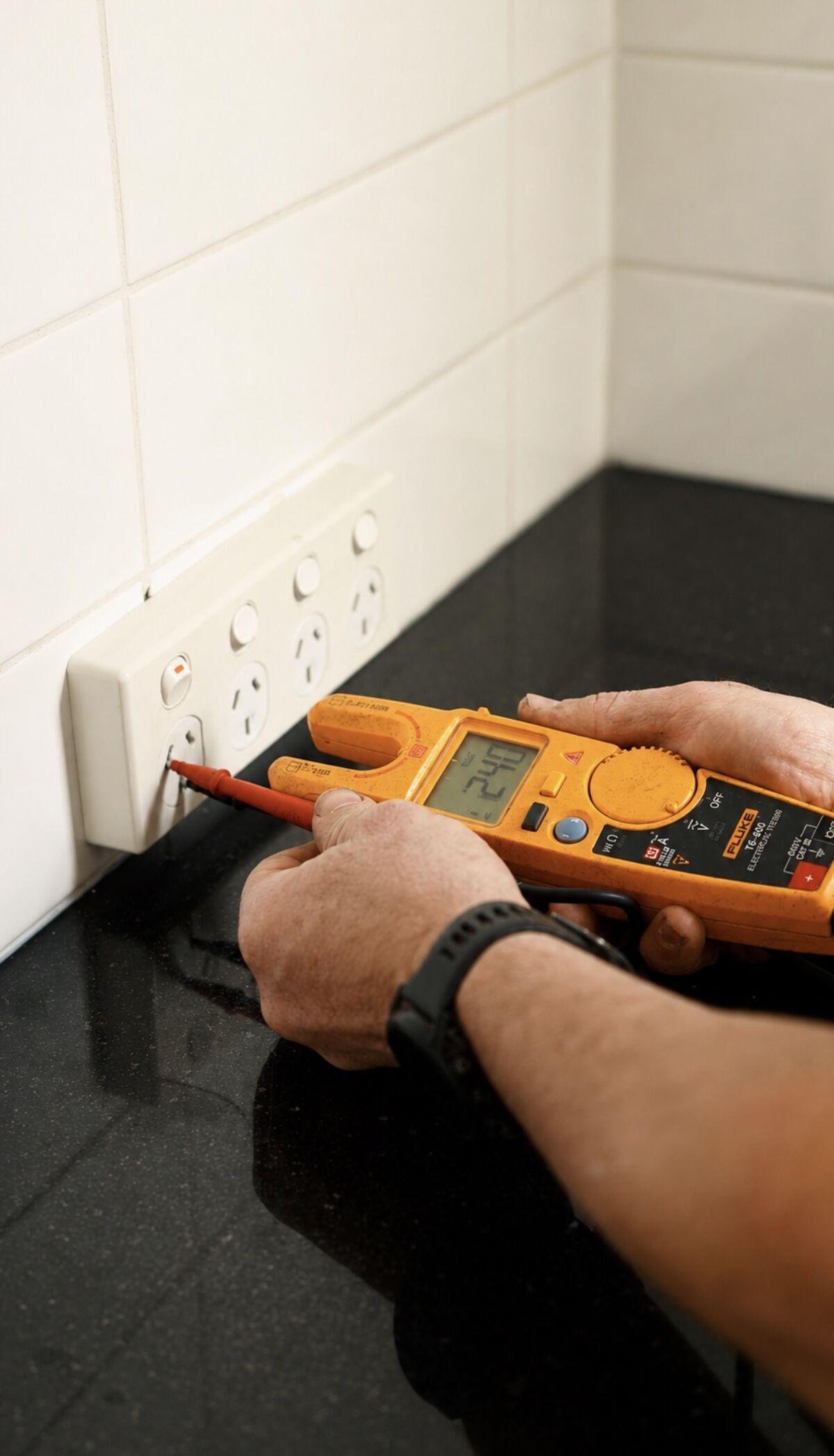 Electrician testing a power point with a clamp meter and test probe