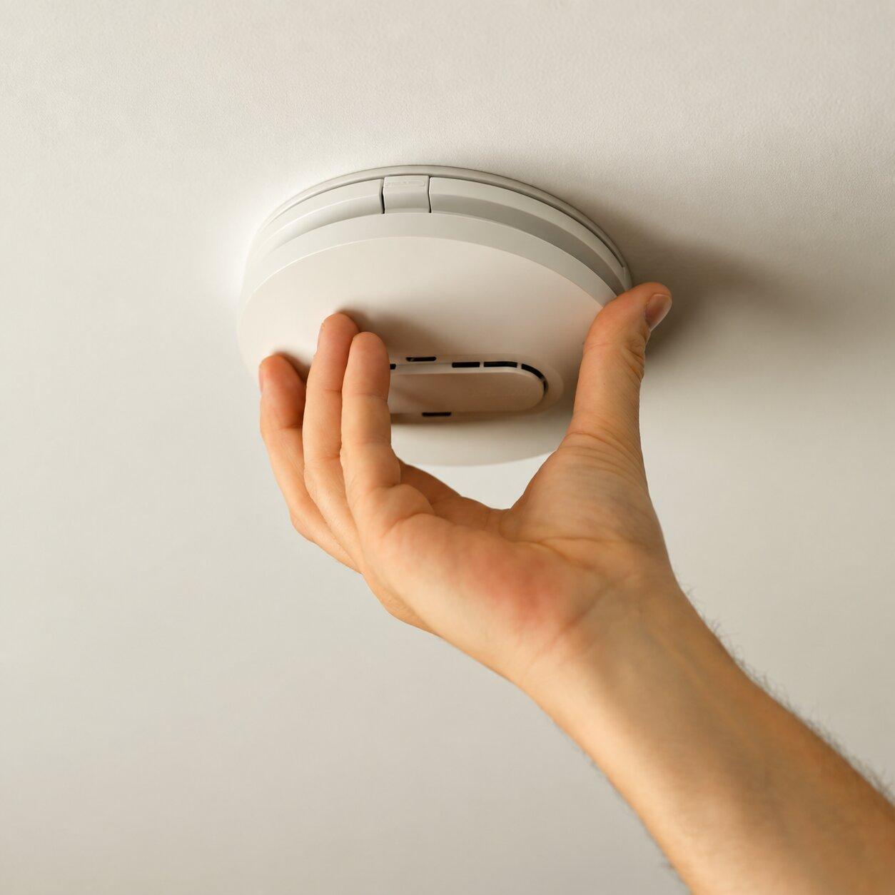 Hand fitting a white smoke alarm to a ceiling