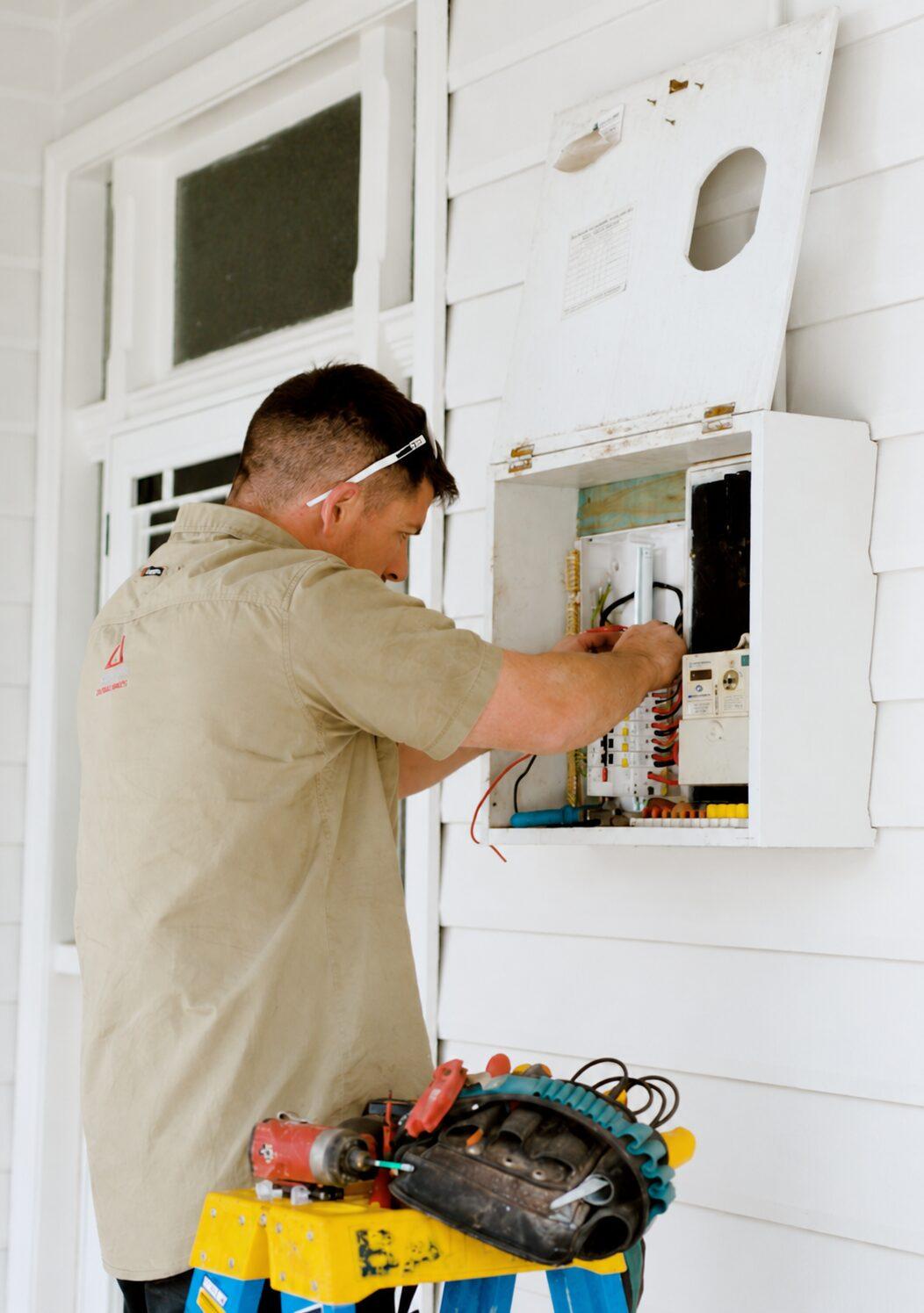 Quantum electrician in a branded shirt wiring new circuit breakers into a home switchboard